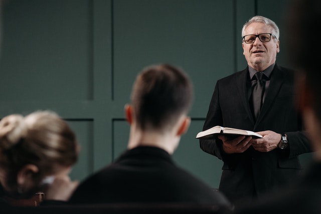Pastor reading a Bible preaches in front of small crowd