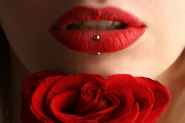 You see the bottom half of a woman's face with red lipstick and a lip piercing hovering seductively over a red rose. Enticing. Sensual. Yum.